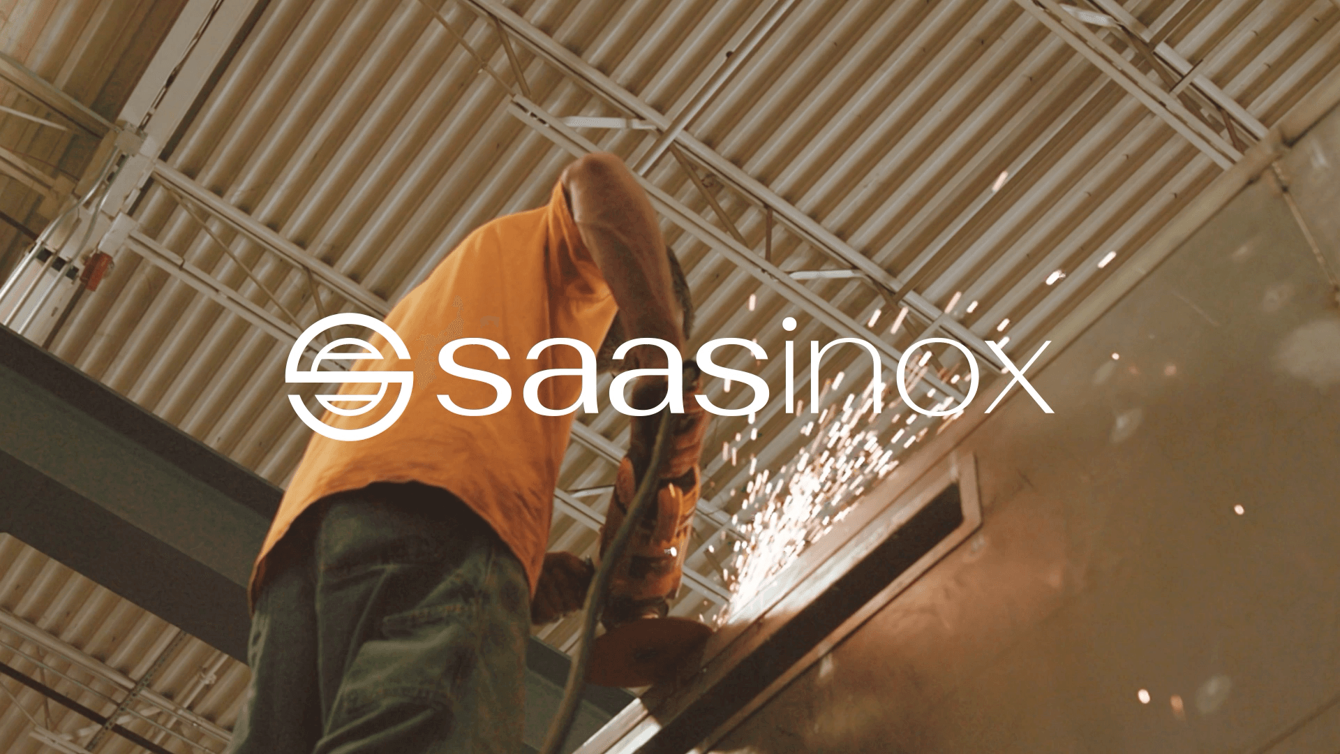 Worker in an orange shirt using an angle grinder on a metal surface, creating bright sparks inside an industrial workshop; overlaid with the Saasinox logo and brand name.