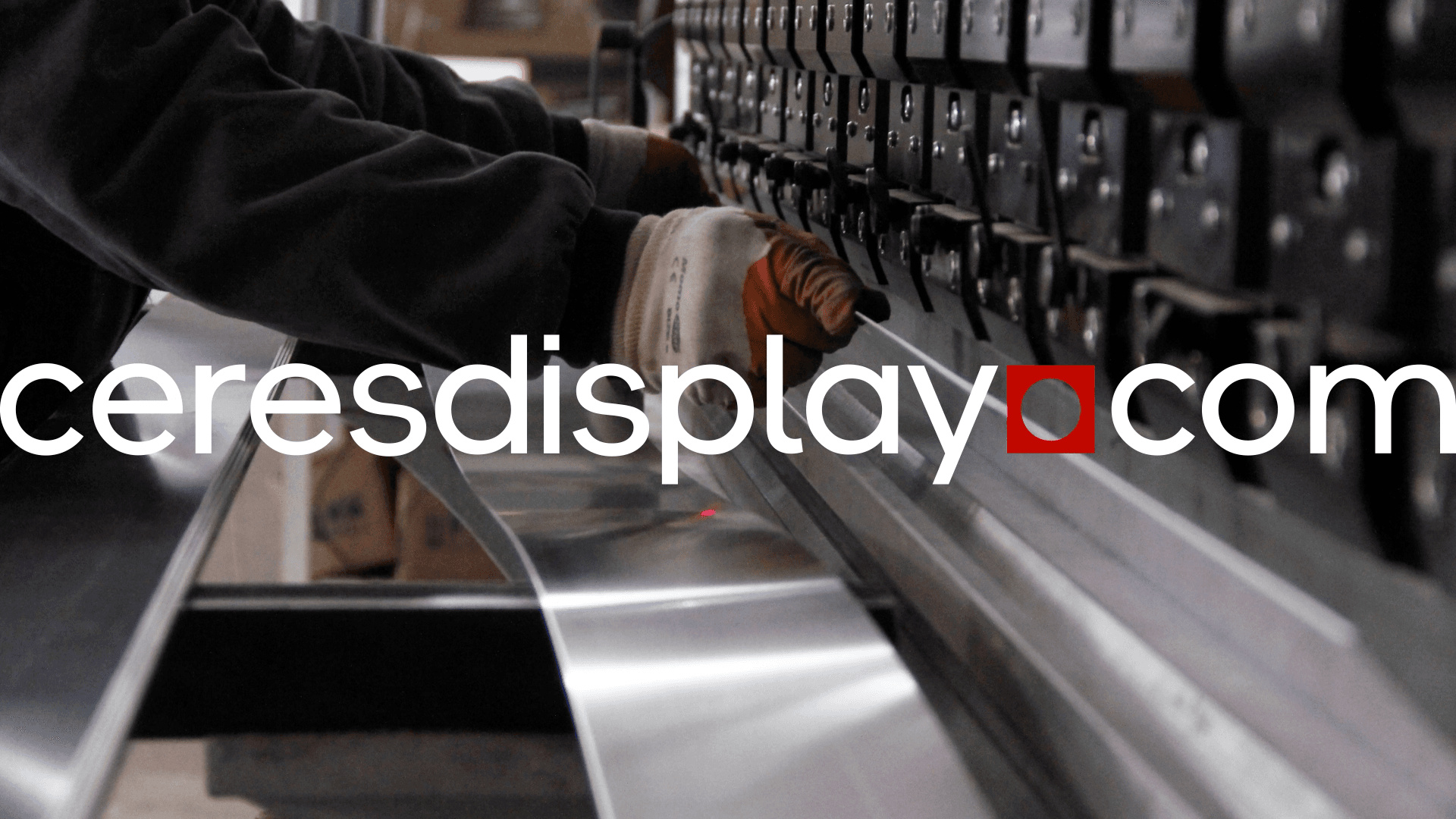 Worker wearing gloves operating an industrial metal bending machine, with the Ceres Display logo and website name ‘ceresdisplay.com’ overlaid on the image.